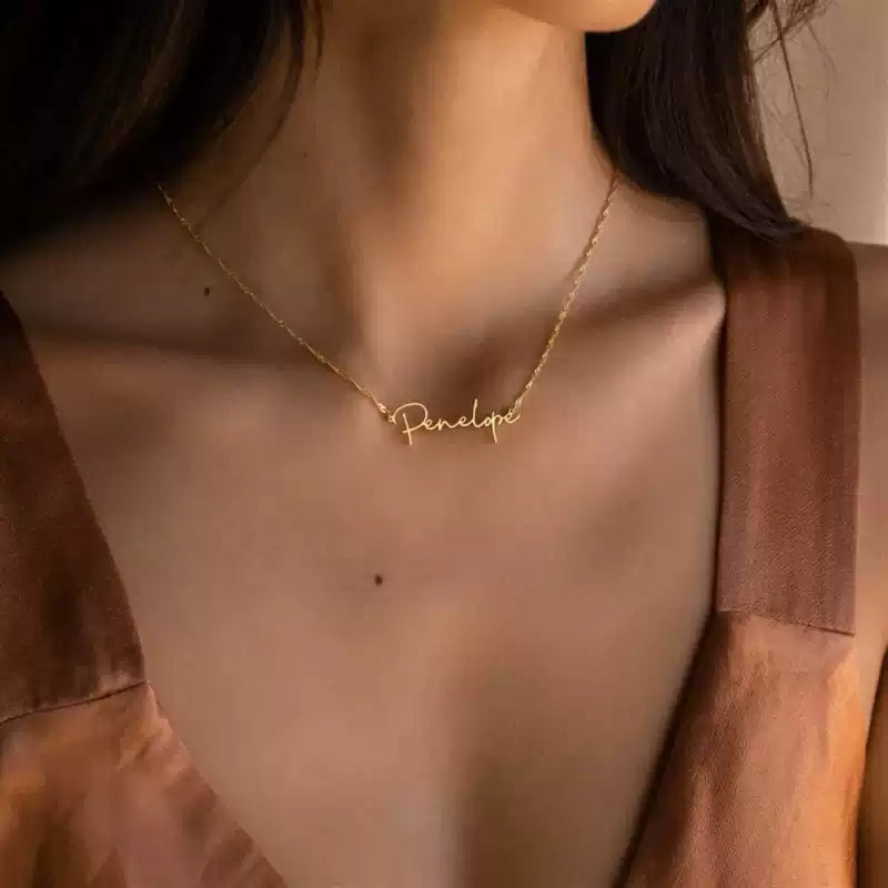 Gold necklace with 'Penelope' on a person wearing a sheer top.. Stainless Steel Name Jewelry. Custom Gift-Personalized. gift for boyfriend / girlfriend. long-distance relationship gift meaningful keepsake. Memory gift. Christmas couple gift. Birthday Gift. Wave Chain Name Necklace