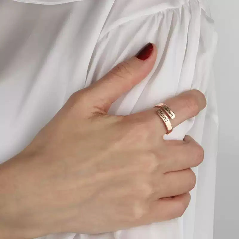 Hand wearing a rose gold ring with engraved text, against a white fabric background. Stainless Steel Name Jewelry. Custom Gift-Personalized. gift for boyfriend / girlfriend. long-distance relationship gift meaningful keepsake. Memory gift. Christmas couple gift. Birthday Gift. Timeless Engrave