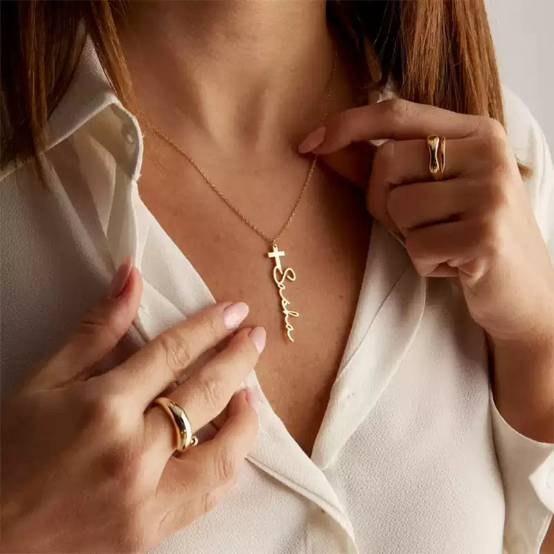 Person wearing a gold necklace with a name pendant and holding a matching ring.. Stainless Steel Name Jewelry. Custom Gift-Personalized. gift for boyfriend / girlfriend. long-distance relationship gift meaningful keepsake. Memory gift. Christmas couple gift. Birthday Gift. Cross Name Necklace