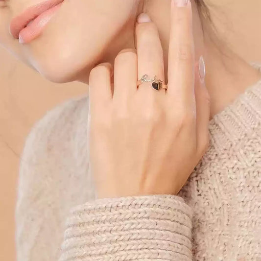 Hand wearing a silver ring with a heart design, wearing a beige sweater. Stainless Steel Name Jewelry. Custom Gift-Personalized. gift for boyfriend / girlfriend. long-distance relationship gift meaningful keepsake. Memory gift. Christmas couple gift. Birthday Gift.