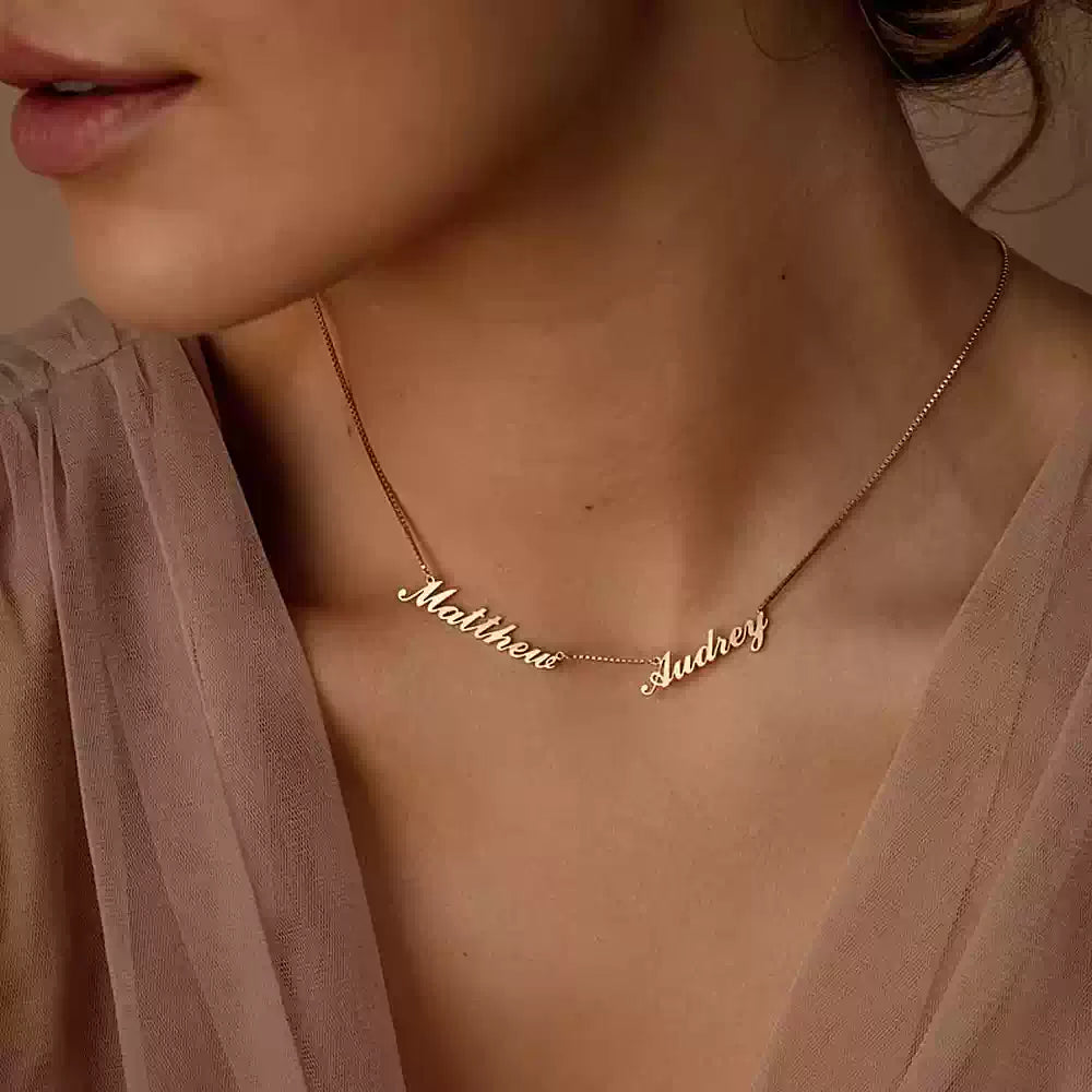 Gold necklace with engraved names on a person wearing a sheer pink top. Name wiht Box Chain
