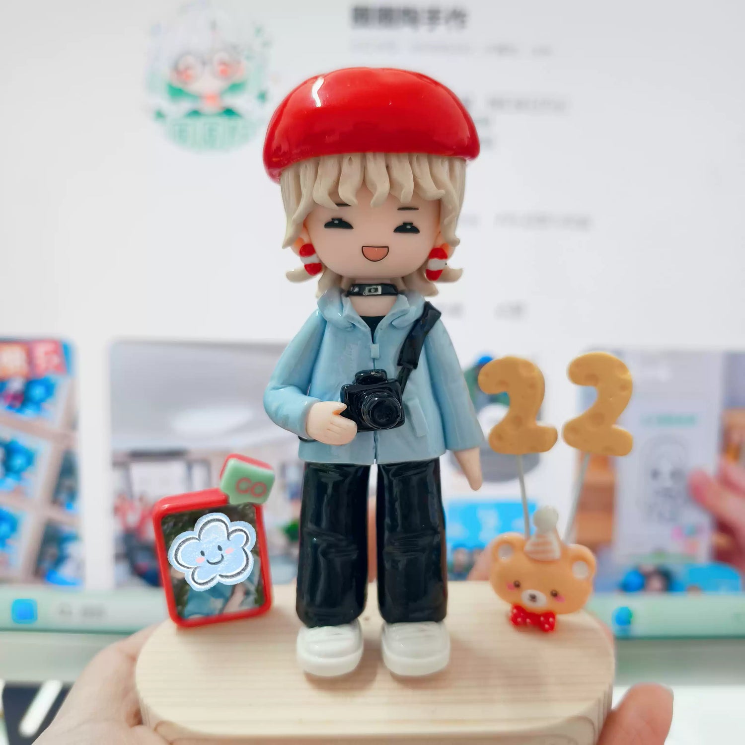 Figurine of a person with a red cap holding a camera, standing on a wooden base with small items around.