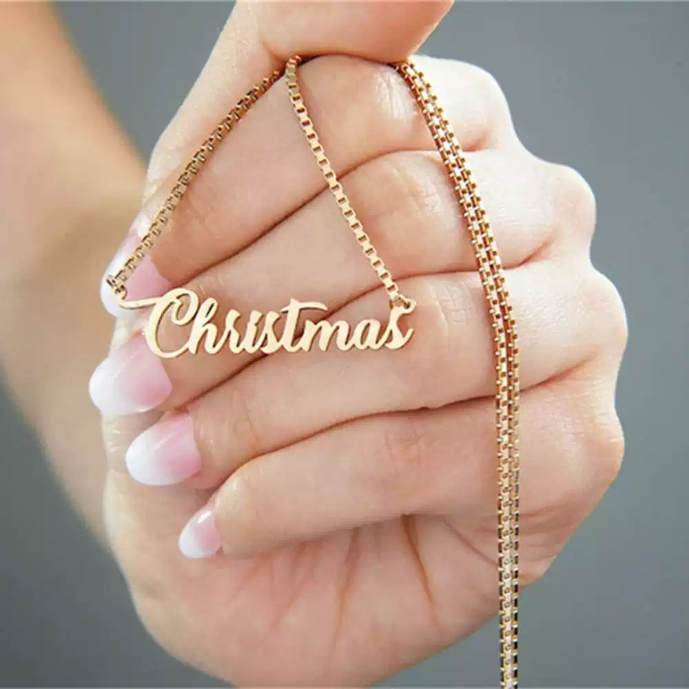 Gold necklace with 'Christmas' pendant held in a hand against a gray Name wiht Box Chainbackground