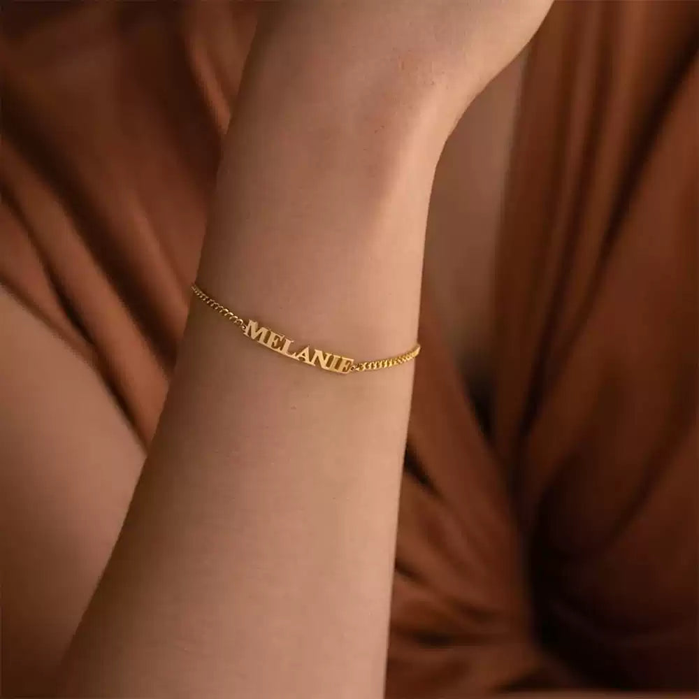 Gold bracelet with 'MELANIE' on a wrist against a brown fabric background. Box Chain. Stainless Steel Name Jewelry. Custom Gift-Personalized. gift for boyfriend / girlfriend. long-distance relationship gift meaningful keepsake. Memory gift. Christmas couple gift. Birthday Gift. 