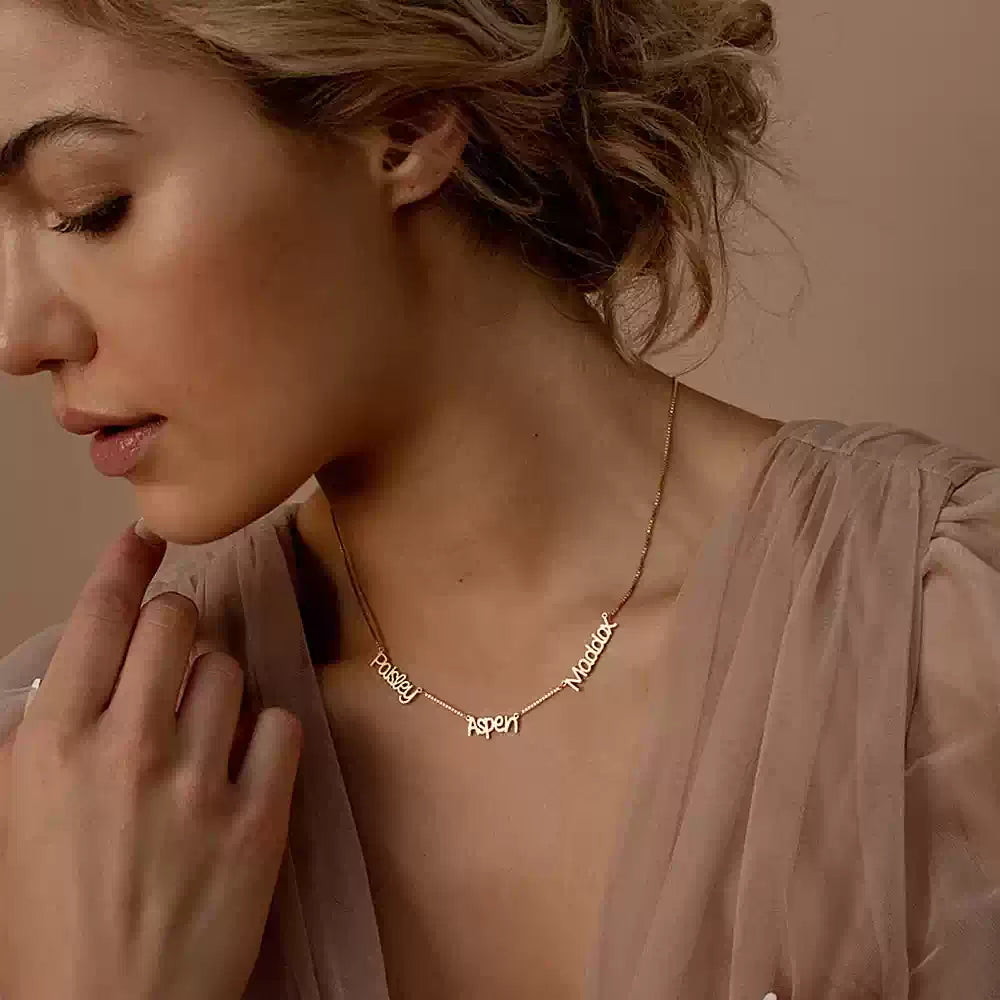 Woman wearing a gold necklace with engraved names against a neutral background. Name wiht Box Chain