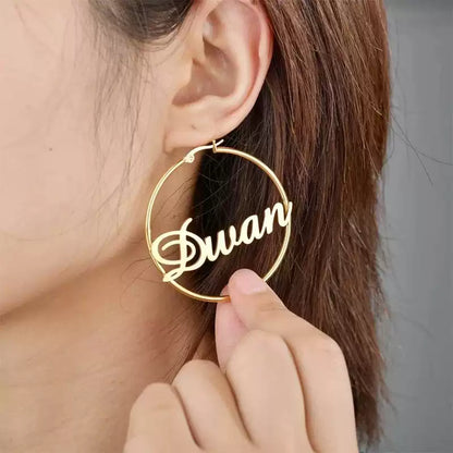 Gold hoop earring with 'Duwan' inscription held near an ear. Stainless Steel Name Jewelry. Custom Gift-Personalized. gift for boyfriend / girlfriend. long-distance relationship gift meaningful keepsake. Memory gift. Christmas couple gift. Birthday Gift. Retro Classic Hoop Name Earrings