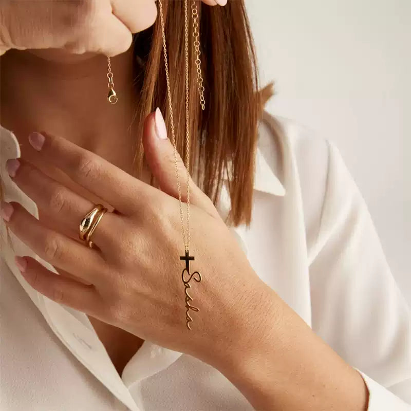 Person wearing a gold necklace with a cross pendant and 'Faith' inscription, holding it near their face.. Stainless Steel Name Jewelry. Custom Gift-Personalized. gift for boyfriend / girlfriend. long-distance relationship gift meaningful keepsake. Memory gift. Christmas couple gift. Birthday Gift. Cross Name Necklace