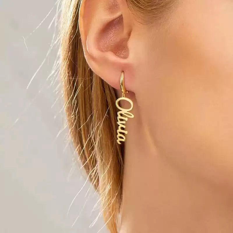 Gold hoop earring with 'Olivia' inscription worn by a person. Stainless Steel Name Jewelry. Custom Gift-Personalized. gift for boyfriend / girlfriend. long-distance relationship gift meaningful keepsake. Memory gift. Christmas couple gift. Birthday Gift. Vertical Charm Ear Cuffs