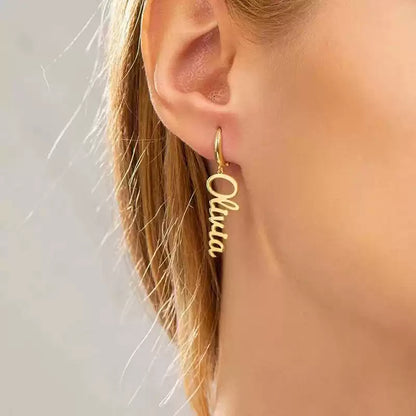 Gold hoop earring with 'Olivia' inscription worn by a person. Stainless Steel Name Jewelry. Custom Gift-Personalized. gift for boyfriend / girlfriend. long-distance relationship gift meaningful keepsake. Memory gift. Christmas couple gift. Birthday Gift. Vertical Charm Ear Cuffs
