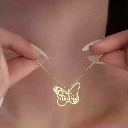 Gold butterfly-shaped necklace with 'Bella' engraved, held by hands against a blurred background.. Stainless Steel Name Jewelry. Custom Gift-Personalized. gift for boyfriend / girlfriend. long-distance relationship gift meaningful keepsake. Memory gift. Christmas couple gift. Birthday Gift. Butterfly & Blossom Name Necklace
