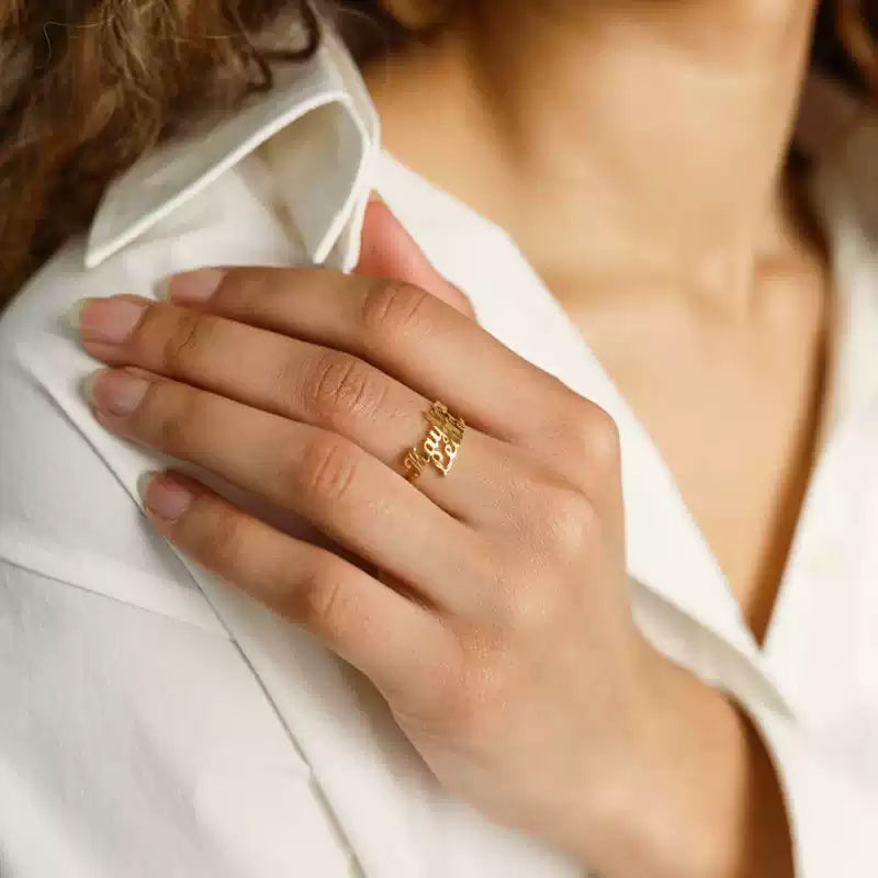 Close-up of a hand wearing a gold ring with a blurred background. 