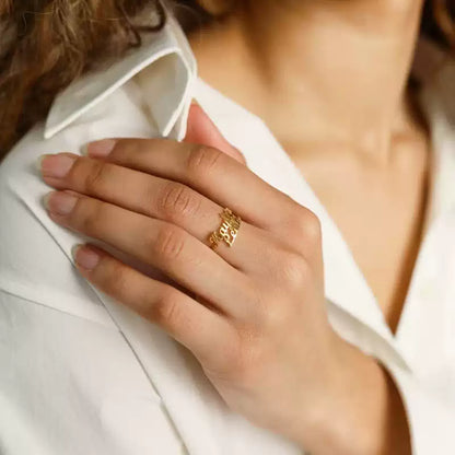 Close-up of a hand wearing a gold ring with a blurred background. 