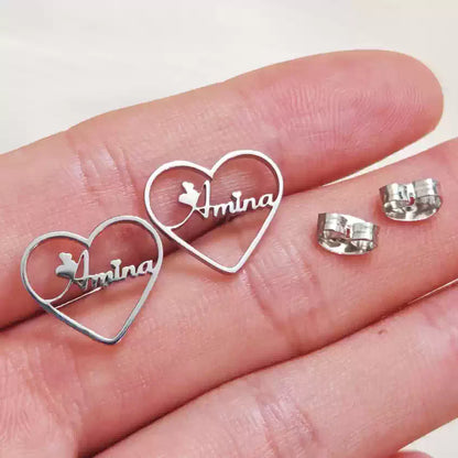 Silver heart-shaped earrings with 'Amina' engraved on a hand. Stainless Steel Name Jewelry. Custom Gift-Personalized. gift for boyfriend / girlfriend. long-distance relationship gift meaningful keepsake. Memory gift. Christmas couple gift. Birthday Gift. Heart Embrace Name Studs 