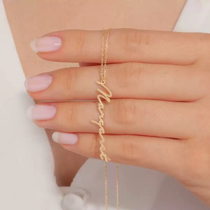 Gold 'Marquesas' necklace on a hand with pink nail polish against a neutral background Stainless Steel Name Jewelry. Custom Gift-Personalized. gift for boyfriend / girlfriend. long-distance relationship gift meaningful keepsake. Memory gift. Christmas couple gift. Birthday Gift. Vertical Name Necklace