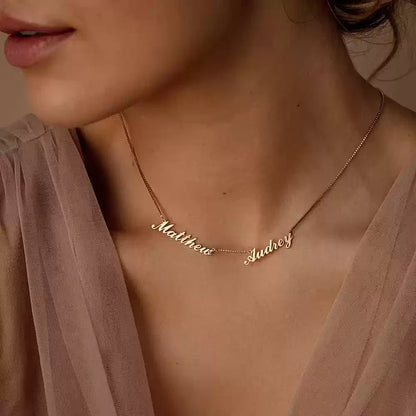Gold necklace with engraved names on a person wearing a sheer pink top. Name wiht Box Chain
