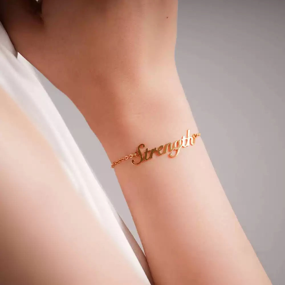Gold 'Strength' bracelet on a person's wrist with a neutral background Stainless Steel Name Jewelry. Custom Gift-Personalized. gift for boyfriend / girlfriend. long-distance relationship gift meaningful keepsake. Memory gift. Christmas couple gift. Birthday Gift. 