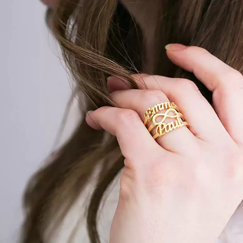 Gold ring with engraved text worn on a finger, held by a hand with brown hair.Stainless Steel Name Jewelry. Custom Gift-Personalized. gift for boyfriend / girlfriend. long-distance relationship gift meaningful keepsake. Memory gift. Christmas couple gift. Birthday Gift. Infinity Embrace
