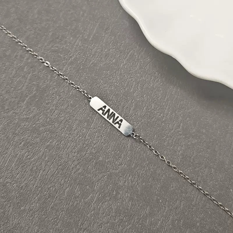 Silver necklace with a bar pendant engraved with 'ANNA' on a gray surface. Hollow Plaque. Stainless Steel Name Jewelry. Custom Gift-Personalized. gift for boyfriend / girlfriend. long-distance relationship gift meaningful keepsake. Memory gift. Christmas couple gift. Birthday Gift. 