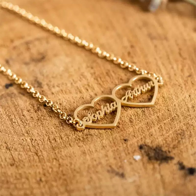 Gold necklace with heart-shaped name pendants on a wooden surface. Double heart. Stainless Steel Name Jewelry. Custom Gift-Personalized. gift for boyfriend / girlfriend. long-distance relationship gift meaningful keepsake. Memory gift. Christmas couple gift. Birthday Gift. 