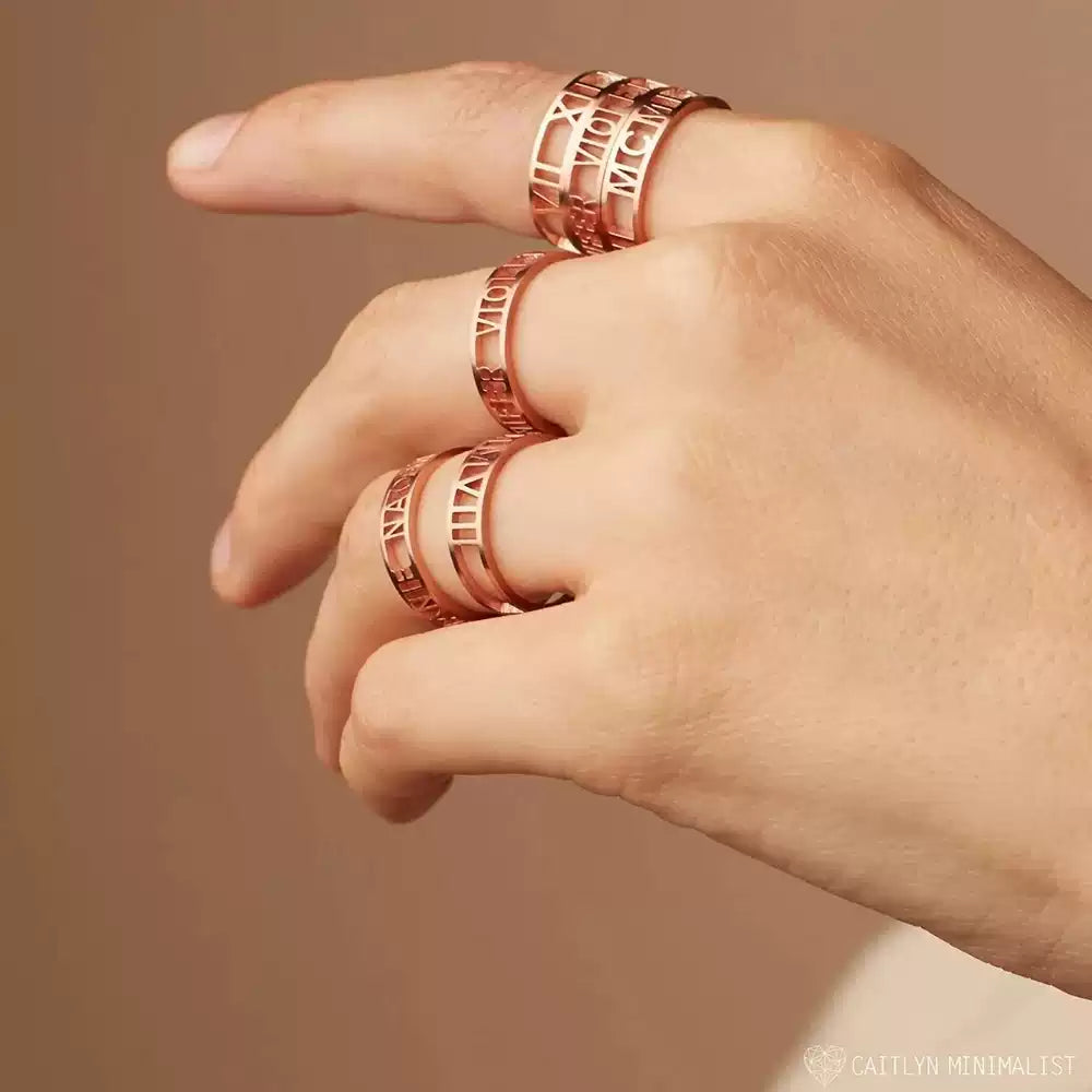 Hand wearing multiple rose gold rings on a beige background. Stainless Steel Name Jewelry. Custom Gift-Personalized. gift for boyfriend / girlfriend. long-distance relationship gift meaningful keepsake. Memory gift. Christmas couple gift. Birthday Gift. Bold Initial Frame