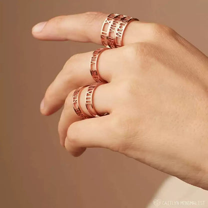 Hand wearing multiple rose gold rings on a beige background. Stainless Steel Name Jewelry. Custom Gift-Personalized. gift for boyfriend / girlfriend. long-distance relationship gift meaningful keepsake. Memory gift. Christmas couple gift. Birthday Gift. Bold Initial Frame