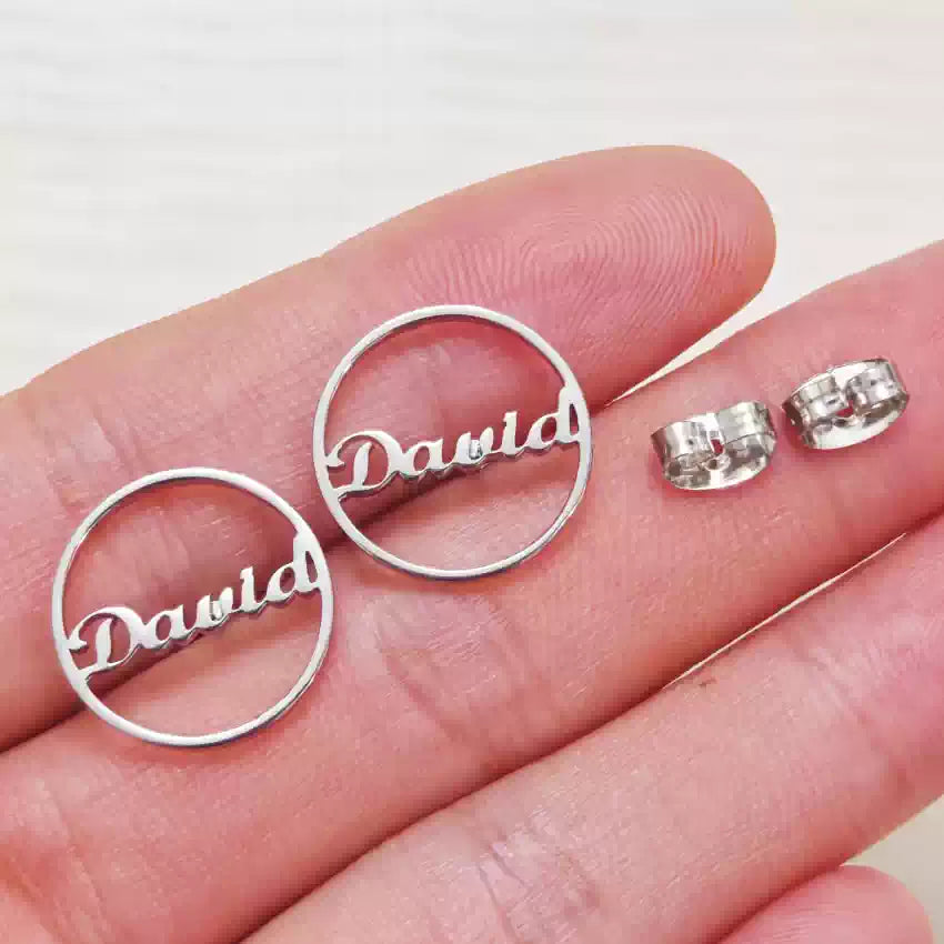 Silver 'David' earrings on a hand against a white background Stainless Steel Name Jewelry. Custom Gift-Personalized. gift for boyfriend / girlfriend. long-distance relationship gift meaningful keepsake. Memory gift. Christmas couple gift. Birthday Gift. Circle Charm Name Earrings