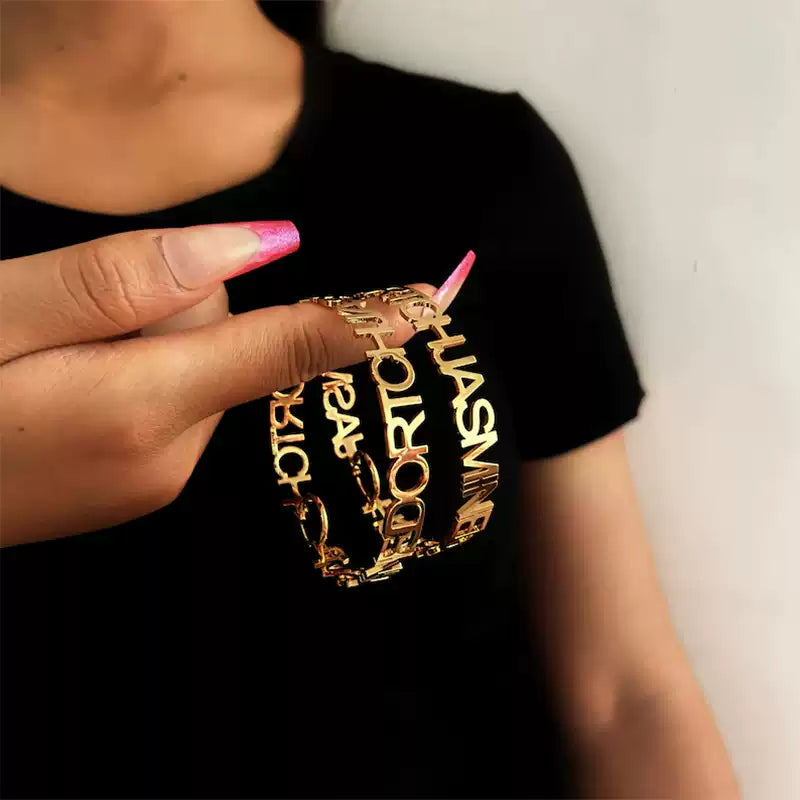 Gold bracelet with text held by a person wearing a black shirt. Stainless Steel Name Jewelry. Custom Gift-Personalized. gift for boyfriend / girlfriend. long-distance relationship gift meaningful keepsake. Memory gift. Christmas couple gift. Birthday Gift. Statement Loop Name Earrings