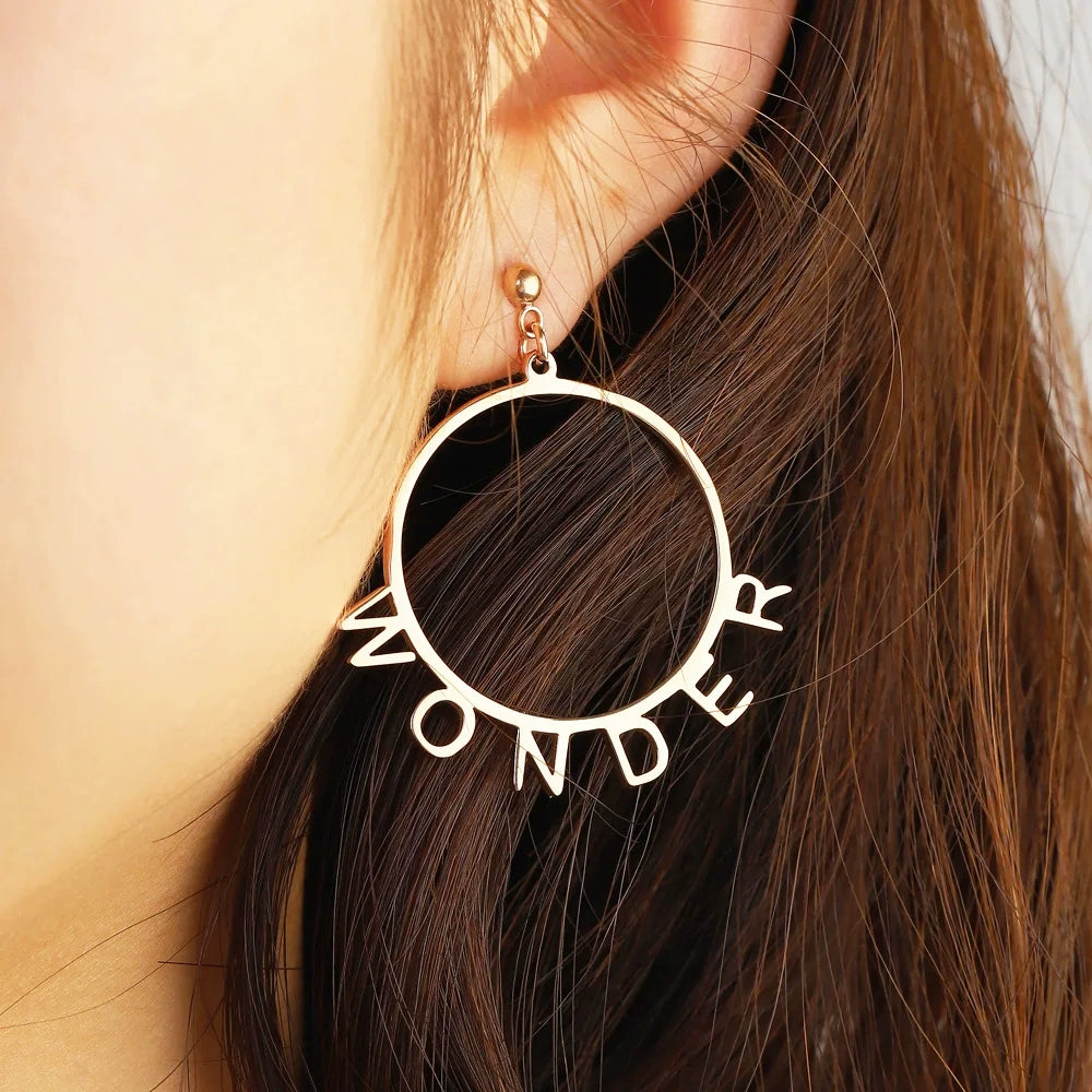 Gold hoop earrings with 'WONDER' design worn by a person with brown hair. Stainless Steel Name Jewelry. Custom Gift-Personalized. gift for boyfriend / girlfriend. long-distance relationship gift meaningful keepsake. Memory gift. Christmas couple gift. Birthday Gift. Playful Circle Name Earrings