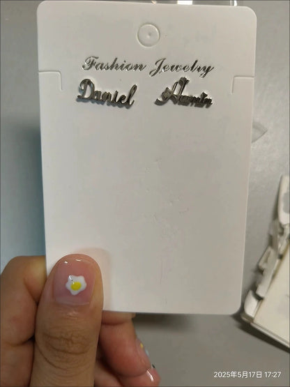 White jewelry tag with 'Fashion Jewelry Daniel Arlen' text held by a hand. Stainless Steel Name Jewelry. Custom Gift-Personalized. gift for boyfriend / girlfriend. long-distance relationship gift meaningful keepsake. Memory gift. Christmas couple gift. Birthday Gift. Curved SoulName Earrings